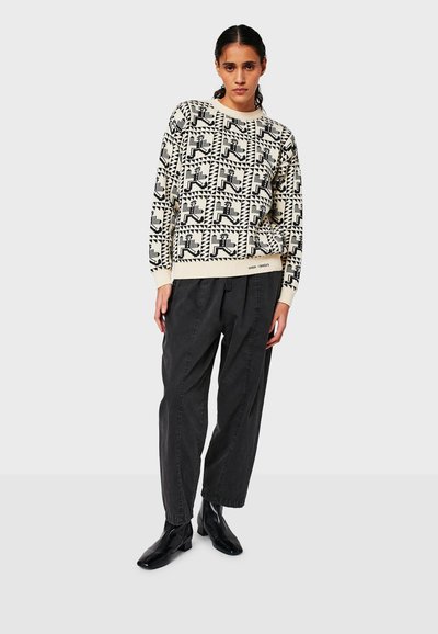 Maglione con motivi geometrici in nero e crema, scollatura rotonda, maniche lunghe. Abbinato a pantaloni neri larghi e stivaletti alla caviglia.