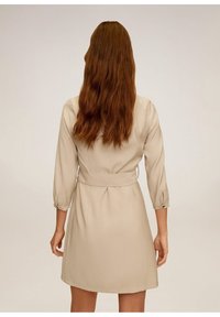 Beiges Kleid mit drei Viertelärmeln, tailliertem Bund und glatter Textur, das oberhalb des Knies fällt, ohne sichtbare Muster oder Verzierungen.