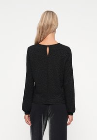 Schwarzes Langarmoberteil mit einem dezenten Leopardenmuster, Rundhalsausschnitt und einem schlüssellochförmigen Detail hinten. Der Stoff wirkt strukturiert und weich.