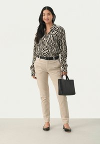 Sort og beige zebra-mønstret bluse med lange ærmer, beige bukser, sort bælte, sort håndtaske og sorte flade sko.
