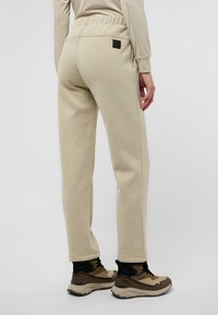 Beige joggingsbroeken met een elastische tailleband, taps toelopende benen en zijzakken. Heeft een klein zwart logo-patch op de achterzak.