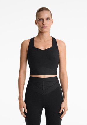 Schwarzes sportliches Crop-Top mit quadratischem Ausschnitt und breiten Trägern, kombiniert mit hochgeschnittenen Leggings mit strukturierten geometrischen Mustern.