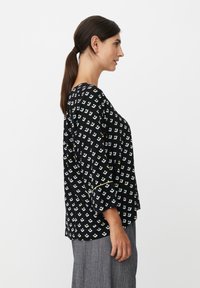 Zwarte blouse met een geometrisch patroon in lichtblauw, wit en geel. De driekwart mouwen zijn voorzien van een contrasterende bies.