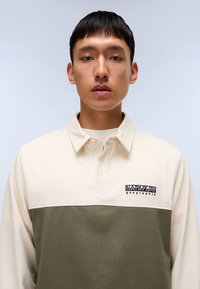 Polo skjorte med en kremfarget overdel og olivengrønn underdel. Laget av en bomullsblanding med brodert logo på brystet.