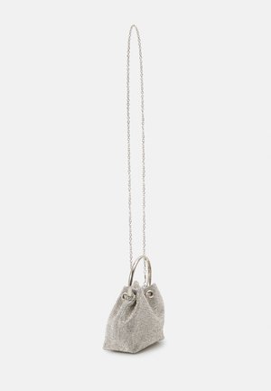 Petit sac à main en maille argentée avec des poignées en anneau métallique et une longue fine chaîne, posé sur un fond uni clair.