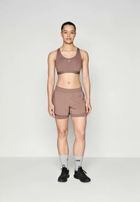 Cet ensemble sportif se compose d'un soutien-gorge de sport marron avec un logo, de shorts marron assortis, de chaussettes grises et de chaussures de course noires. Texture de tissu lisse.