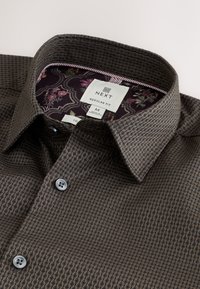 Dark brown shirt with a textured, honeycomb pattern. Features a button-down collar, gray buttons, and a floral patterned inner lining.
