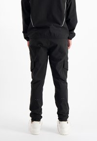 Zwarte cargobroek met zijzakken, verstelbare enkelmanchetten en subtiele branding op het onderbeen. Soepele, lichte stof.