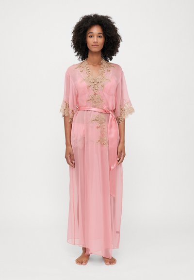 Robe longue en satin rose avec texture transparente, accents en dentelle le long des manches et du col, taille ceinturée et design fluide.