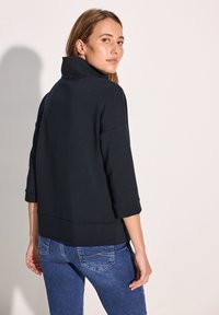 Pullover blu scuro con colletto alto e maniche a tre quarti, realizzato in un tessuto liscio, presenta una vestibilità rilassata e un orlo abbassato.