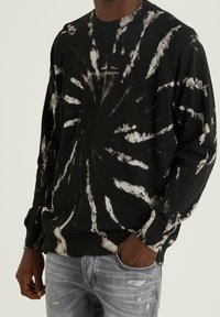Sudadera negra con patrones de tie-dye blancos, cuello redondo, puños y dobladillo acanalados. Fabricada con un material textil suave.