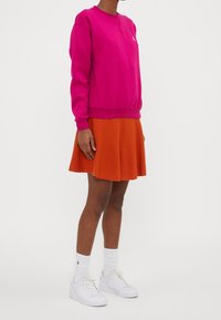 Fuchsiarosa sweatshirt med rund hals och ribbade muddar kombinerad med en orange utsvängd kjol. Vita sneakers och vita crewstrumpor fulländar looken.