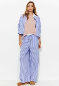 Ensemble de pyjama rayé bleu et blanc avec une chemise à manches courtes et un pantalon à cordon, confectionné en tissu léger, associé à des pantoufles beiges.