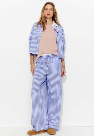 Ensemble de pyjama rayé bleu et blanc avec une chemise à manches courtes et un pantalon à cordon, confectionné en tissu léger, associé à des pantoufles beiges.