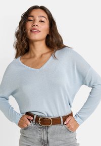 Un haut tricoté à manches longues bleu clair avec un col en V et une coupe décontractée. Associé à un jean taille haute gris et une ceinture marron avec une boucle dorée.