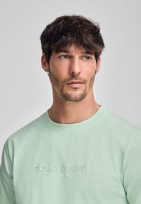 Mintgrön bomullströja med ett präglat logo "POLO CLUB ESTABLISHED 2012" på framsidan, rund hals och mjuk textur.