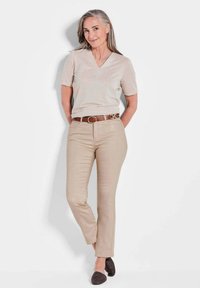Beige V-Ausschnitt-T-Shirt mit kurzen Ärmeln, kombiniert mit hellbeigen, maßgeschneiderten Hosen und einem braunen Gürtel. Die Schuhe sind dunkel und haben ein strukturiertes Design.