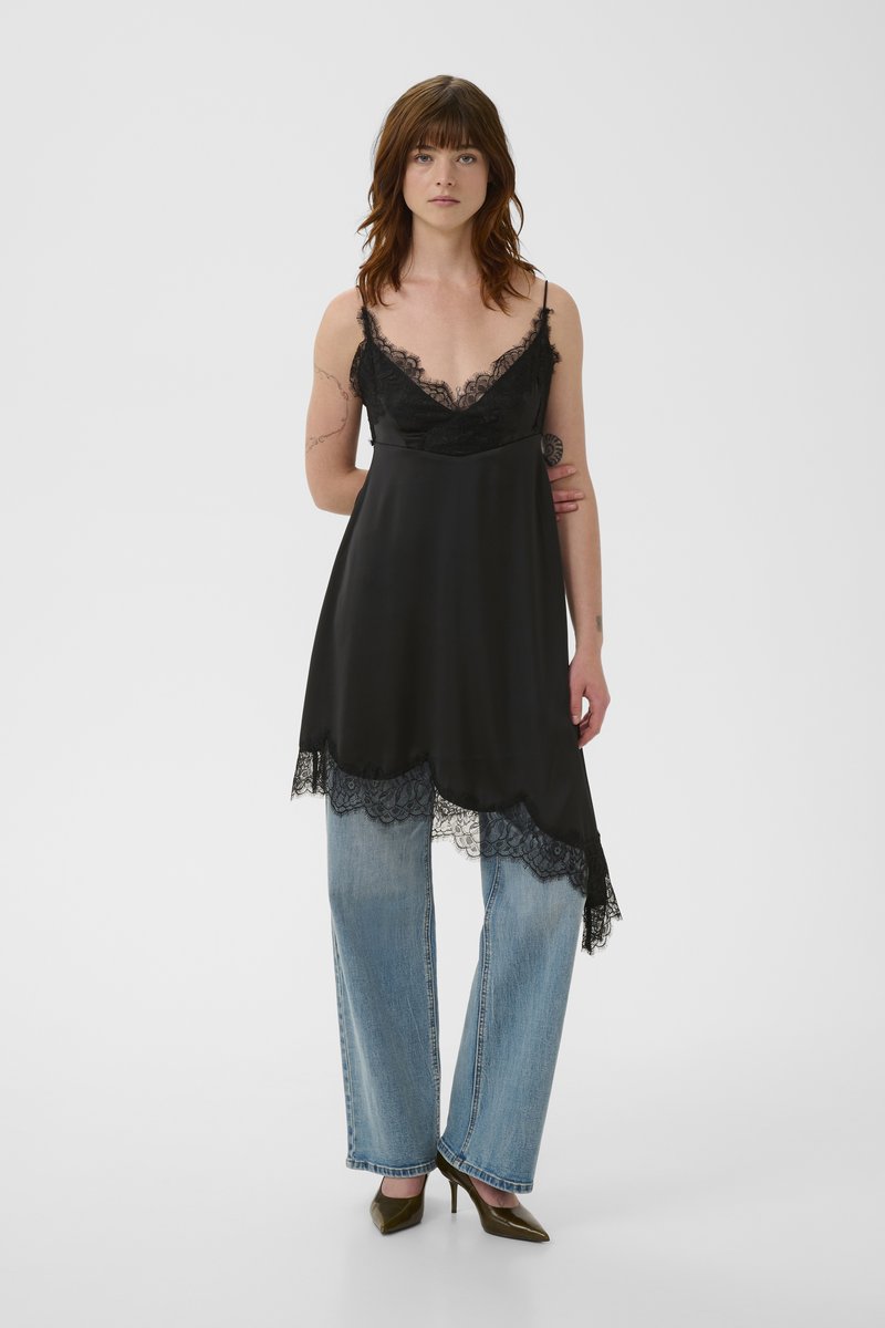 Robe nuisette en satin noir avec bordure en dentelle, présentant un décolleté en V et un ourlet festonné, associée à un jean large bleu clair et des talons olive.