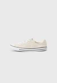 Beige canvas sneaker with white laces, rubber toe cap, black stripes along the sole, and a textured finish on the upper.