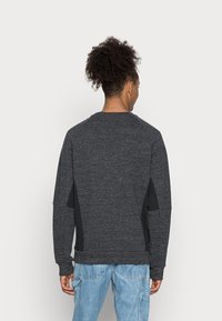 Jersey gris oscuro con mangas raglán, tejido texturizado y paneles laterales negros. Corte casual con cuello redondo y puños acanalados.