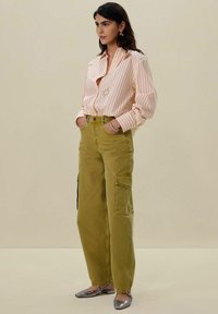 Chemise à rayures pêche et blanche, associée à un pantalon cargo vert olive avec des poches latérales. Des ballerines argentées et de simples boucles d'oreilles complètent le look.