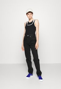 Jeans negros de cintura alta, ajustados en la cintura con pierna recta. Top negro sin mangas con detalles de escote blanco. Gorra blanca, zapatillas deportivas azules.