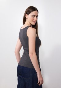 Top grigio senza maniche dal design aderente, con scollatura rotonda e spalline sottili, abbinato a jeans a gamba larga blu scuro. Tessuto liscio, senza motivi visibili.