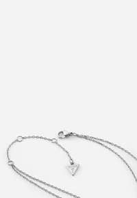 Zilveren ketting met een driehoekige hanger waarop het gegraveerde logo "GUESS?" te zien is, met een karabijnsluiting en meerdere kettinglengtes.