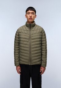 Giacca a vento trapuntata verde oliva con colletto alto e zip centrale. Dettagli a coste sulle spalle, abbinata a pantaloni cargo neri.