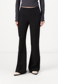 Μαύρο φαρδύ παντελόνι φτιαγμένο από λεία ύφανση, με μπροστινές ραφές και κομψή εφαρμογή. Συνδυάζεται με μπεζ παπούτσια με尖尖尖ο.