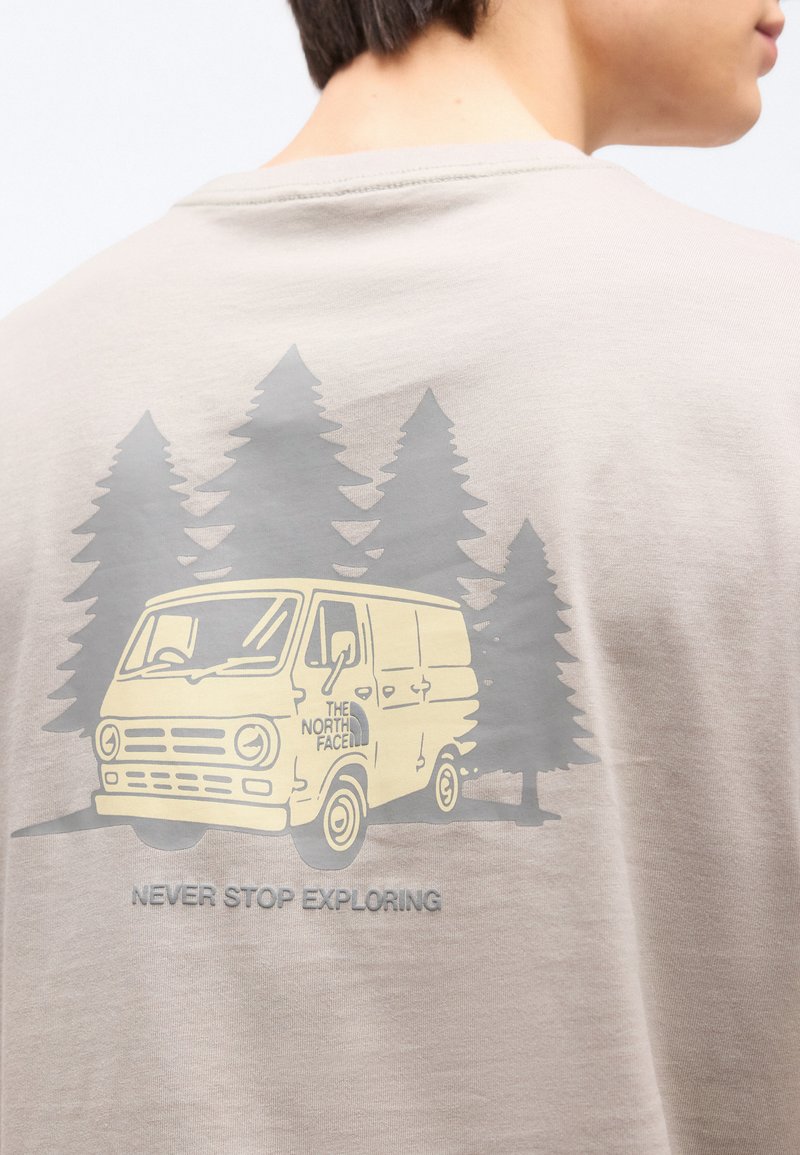Beige shirt showing a yellow van with "The North Face" logo in front of gray pine trees, with "Never Stop Exploring" text below.