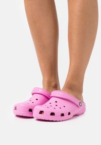 Pink rubber clogs with a closed toe design, ventilation holes, and a back strap. Textured sole and logo on the side.