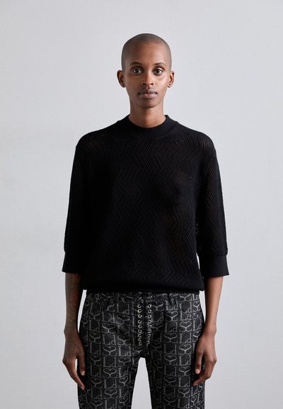 Maglione nero a maglia testurizzata con scollo rotondo e maniche a tre quarti, abbinato a pantaloni scuri a fantasia con un dettaglio di lacci.