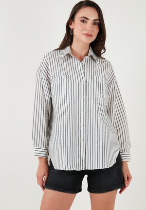 Striped button-up shirt in white and navy, featuring two chest pockets, long sleeves with cuffs, and a relaxed fit. Soft fabric texture.