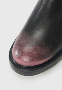 Gros plan sur une chaussure en cuir noir à bout arrondi avec un dégradé subtil violet près de l'avant, dotée d'une semelle épaisse en caoutchouc noir.