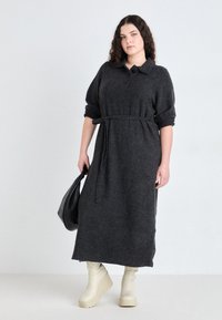 Rochie tricotată gri închis, cu guler, talie definită printr-un brâu și mâneci lungi. Asortată cu cizme crem cu platformă. Accesoriu: geantă neagră.