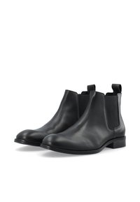 Botas Chelsea negras de cuero con paneles laterales elásticos, punta redondeada y tacón bajo apilado, con una textura suave y un diseño minimalista.
