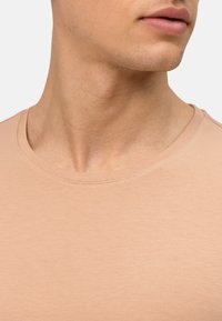 Lichtbeige katoenen t-shirt met een ronde halsontwerp, een gladde textuur en kleine stiksels rond de halslijn en schouders.