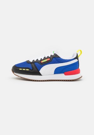 Baskets Puma bleues, noires et blanches avec lacets blancs, accent rouge au talon, languette jaune et semelle gomme sur fond blanc.