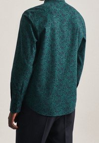 Camicia a maniche lunghe in teal scuro con un motivo floreale, realizzata in un tessuto morbido. Caratterizzata da un polsino con bottoni e un colletto classico. Visuale posteriore mostrata.