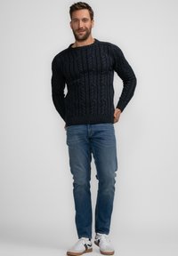Marineblauer Kabelstrickpullover aus strukturiertem Stoff, mit rundem Ausschnitt und gerippten Bündchen, kombiniert mit hellblauen Jeans und weißen Sneakers.