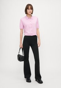 Blusa a maglia rosa a maniche corte con colletto e bottoni, abbinata a pantaloni neri a campana. Borsa nera con forma arrotondata e tracolla.