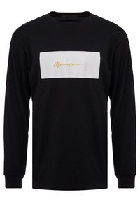 Schwarzes Langarm-T-Shirt aus Baumwolle mit einem weißen rechteckigen Patch, der in der Mitte ein goldenes Signaturdesign aufweist.