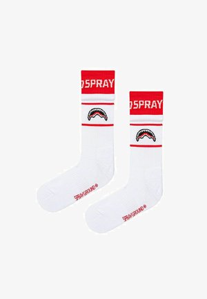 Calzini bianchi con bande rosse in alto, con testo "SPRAY", grafica della bocca di uno squalo sul polpaccio e testo "SPRAYGROUND" vicino alle dita dei piedi.