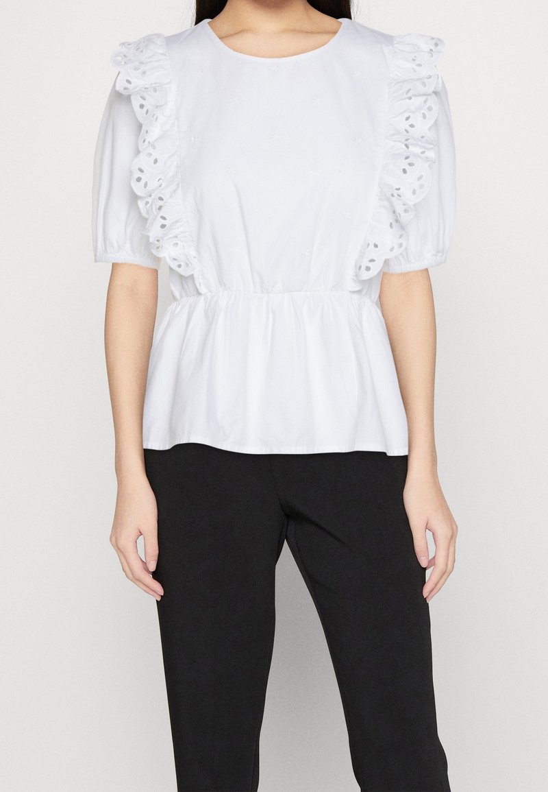 Weiße Bluse mit Rüschensleeves und bestickten Details, mit taillierter Taille und lässigem Schnitt. Dazu schwarze Hosen.