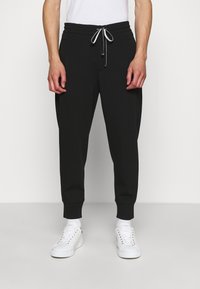 Svarta sweatpants med dragsko i midjan, smalnande ben och cuffade anklar. Tillverkade av ett mjukt material, lämpliga för avslappnad klädsel.