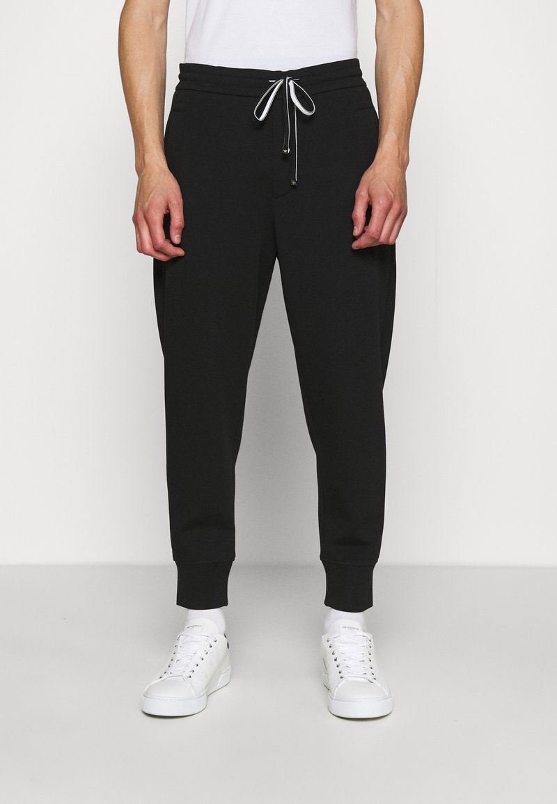 Svarta sweatpants med dragsko i midjan, smalnande ben och cuffade anklar. Tillverkade av ett mjukt material, lämpliga för avslappnad klädsel.