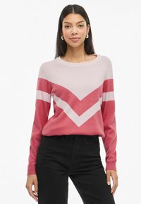 Megztinis su zigzago raštu ro�žinės ir raudonos spalvų deriniu, apykaklė su apvaliu iškirpimu ir ilgos rankovės, derinamas su juodomis džinsais.