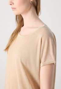 Lichtbeige T-shirt met korte mouwen en een ronde hals, gemaakt van een zachte, licht gestructureerde stof. Heeft een subtiele glans en omgeslagen mouwen.