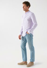 Camisa de botón de color púrpura claro con cuello de banda, combinada con jeans azul claro y alpargatas beige. Textura lisa, ajuste casual.